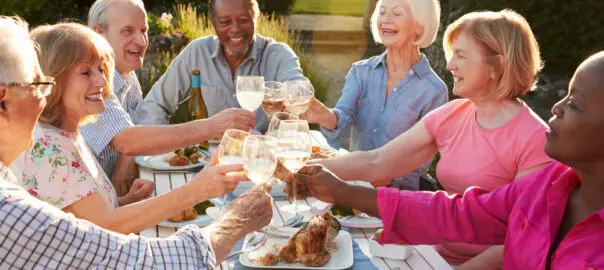 A group of older adults sitting around a picnic table, enjoying dinner with friends.